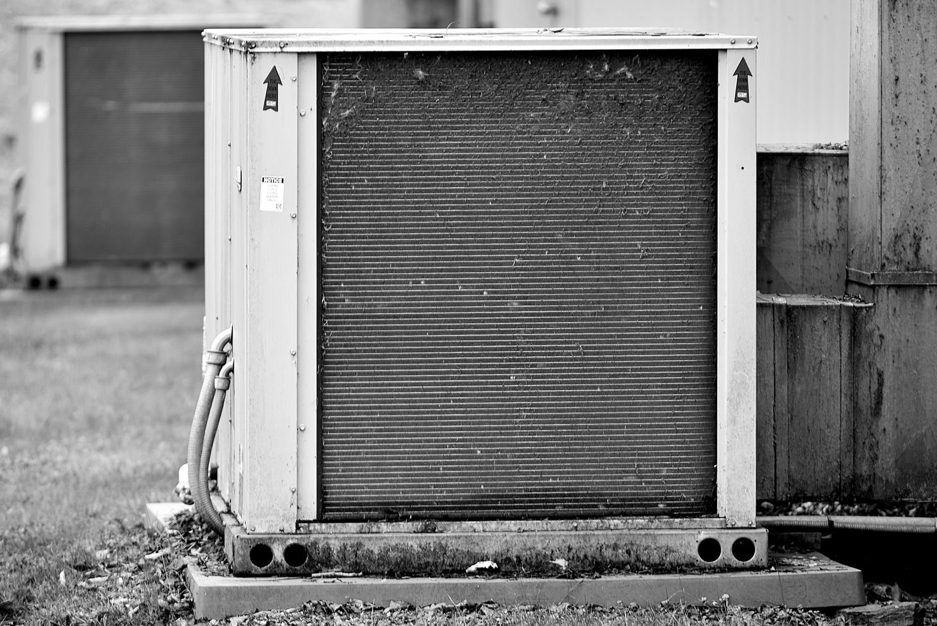 Black and white photo of a weathered commercial condensing unit on a concrete pad, its coil face dusty, with conduit running into the side