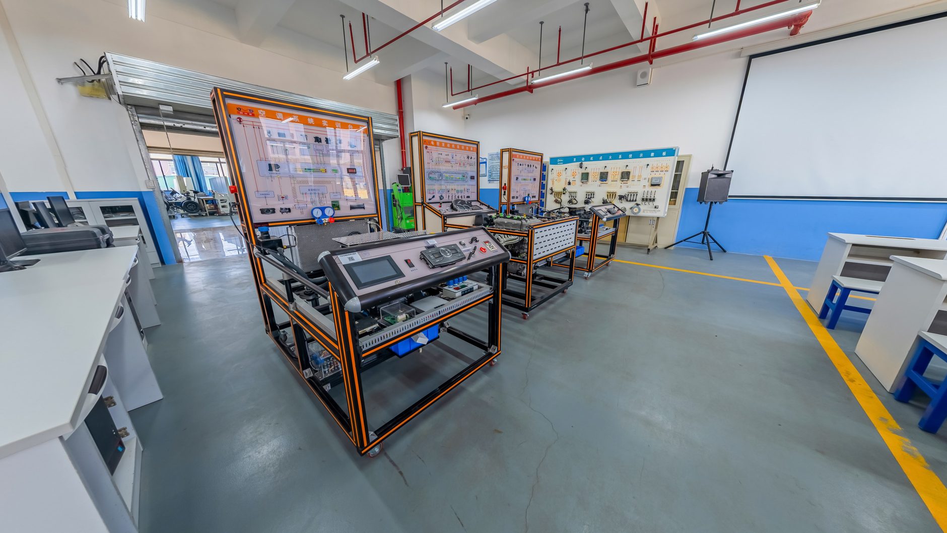A technical training lab with an air conditioning system trainer on a wheeled frame, a control console and wall-mounted system diagrams