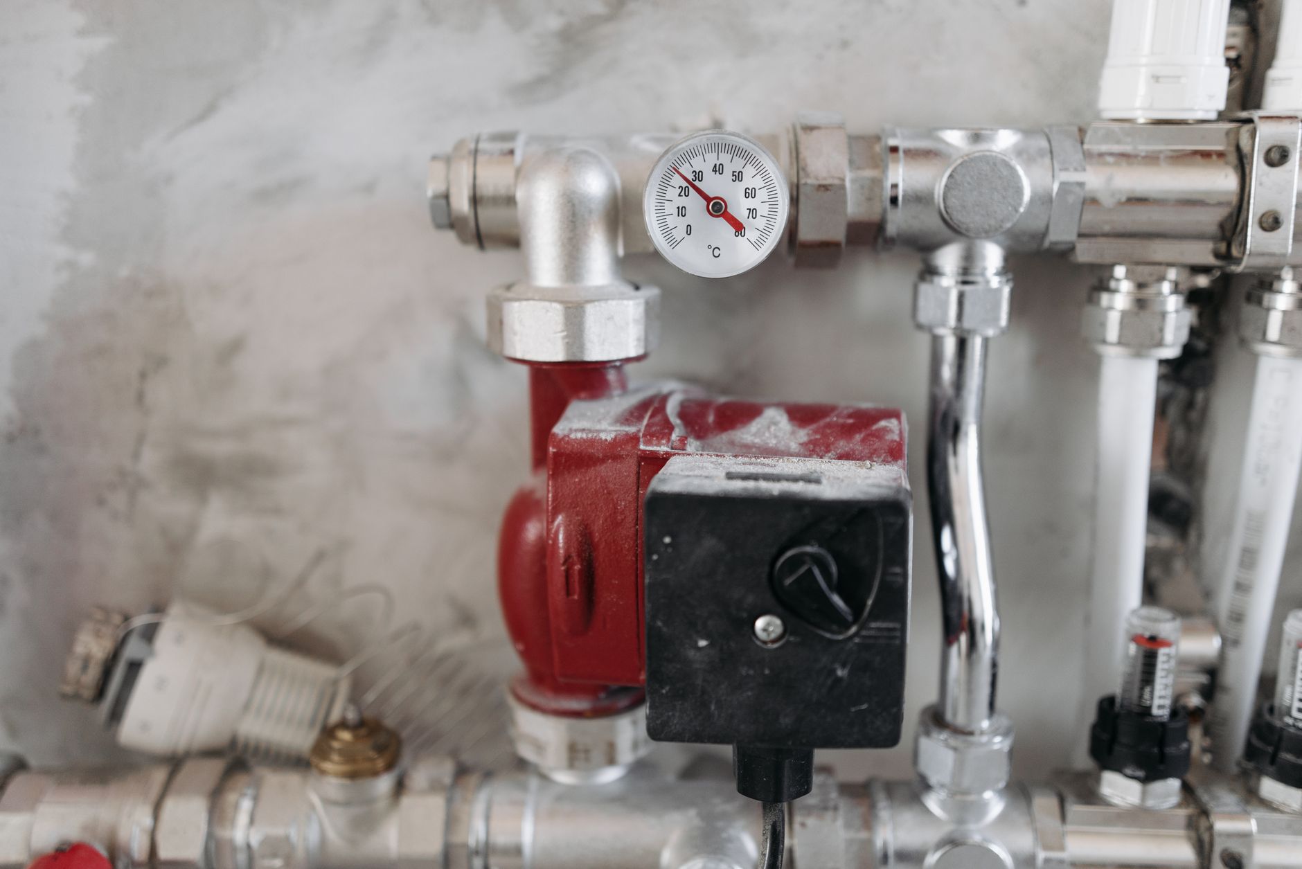 Close-up of a hydronic heating manifold with a red circulator pump, chrome pipe fittings and a round temperature gauge