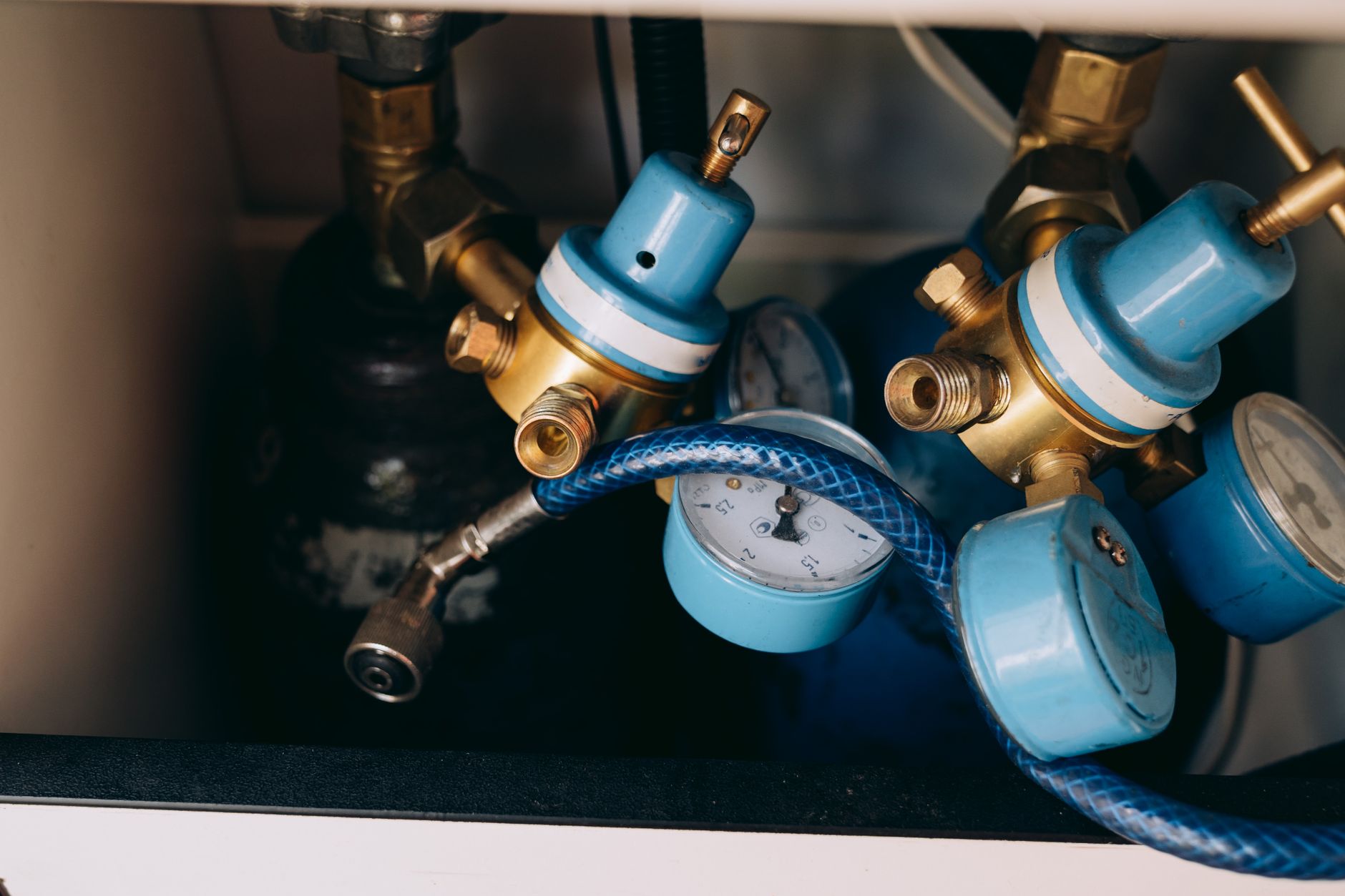 Blue and brass pressure regulators with round dial gauges and a braided blue hose mounted on gas cylinders inside a cabinet