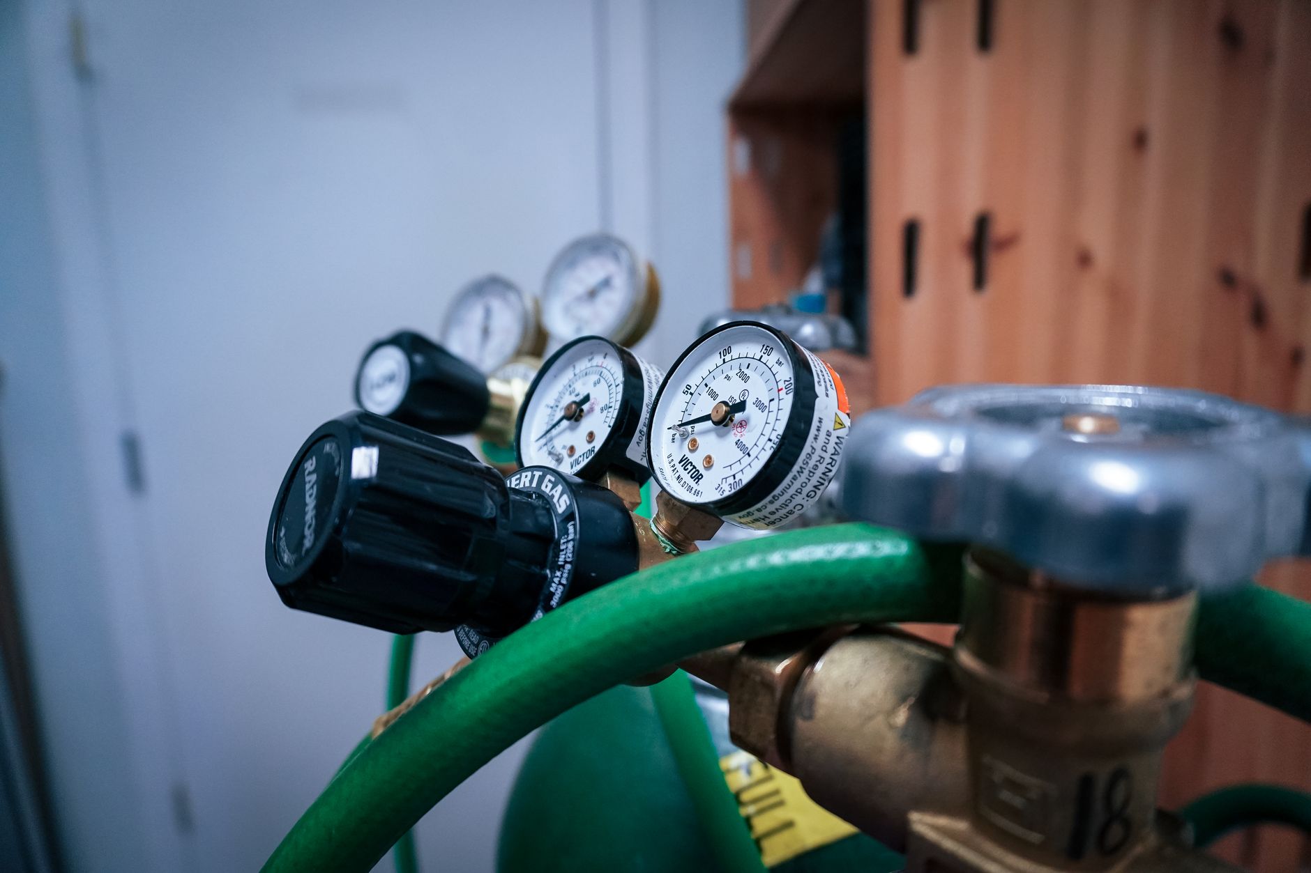 Close-up of brass gas pressure regulators with round dial gauges and a green hose on a cylinder in a workshop