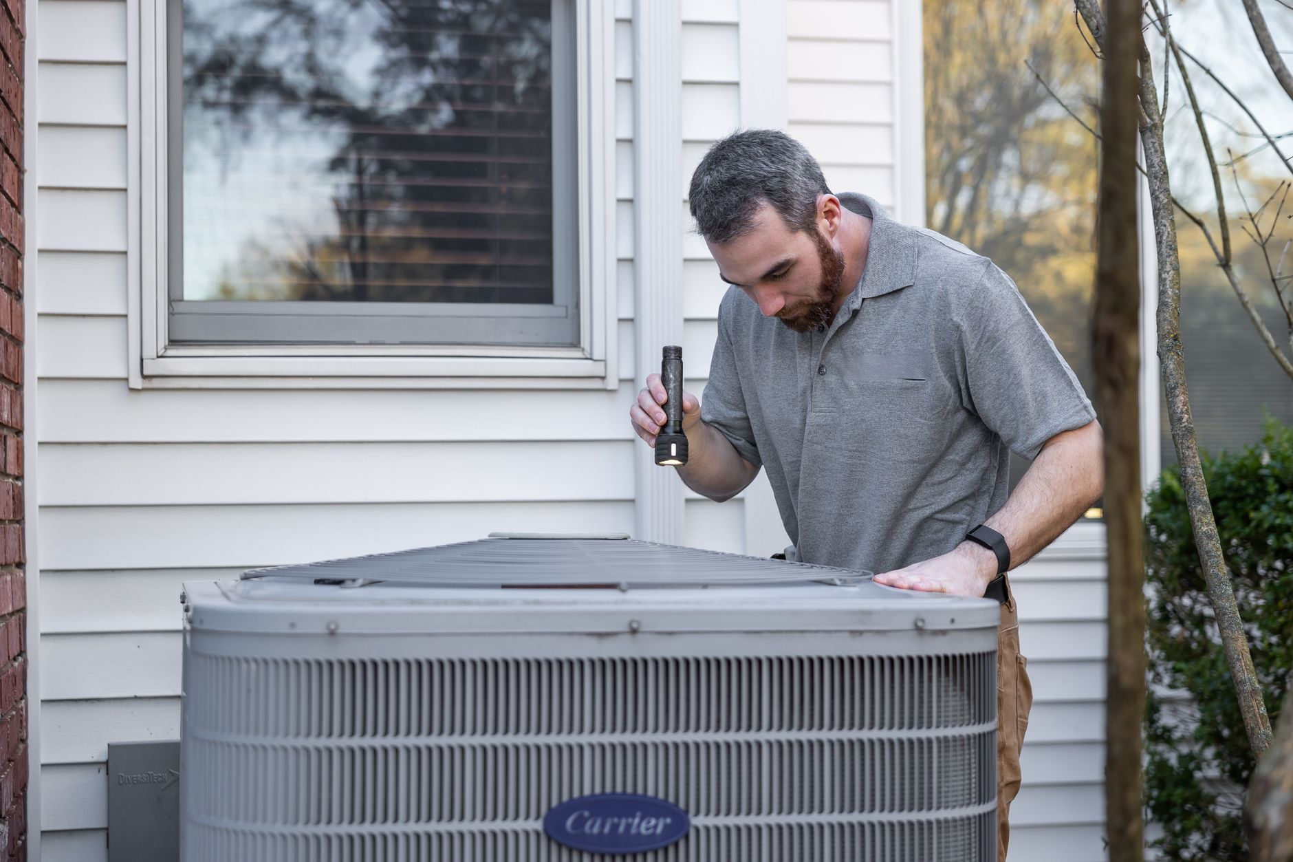 A technician shining a flashlight into the top of a home's outdoor air conditioning unit